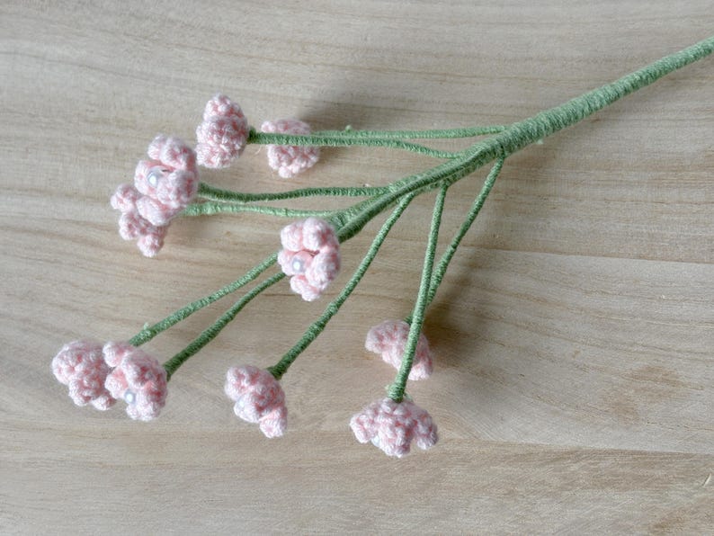May include: A bouquet of pink crocheted flowers with green stems. The flowers have a pearl-like center.