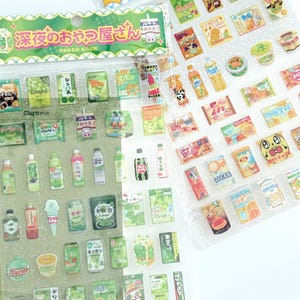 May include: Two sheets of Japanese-style stickers featuring various food and drink illustrations. The stickers include images of snacks, beverages, and desserts in vibrant colors. The packaging has Japanese text and decorative elements, perfect for scrapbooking or crafting.