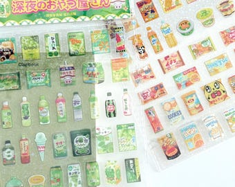 May include: Two sheets of Japanese-style stickers featuring various food and drink illustrations. The stickers include images of snacks, beverages, and desserts in vibrant colors. The packaging has Japanese text and decorative elements, perfect for scrapbooking or crafting.