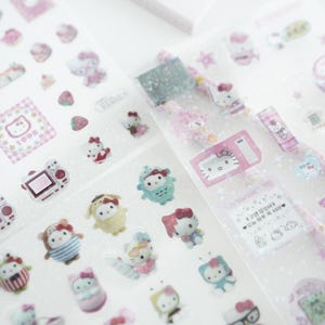 May include: A sheet of clear stickers featuring a variety of Hello Kitty characters. The stickers are pink, white, and blue and feature Hello Kitty in different poses and outfits. The stickers are perfect for adding a touch of whimsy to your planner, journal, or scrapbook.