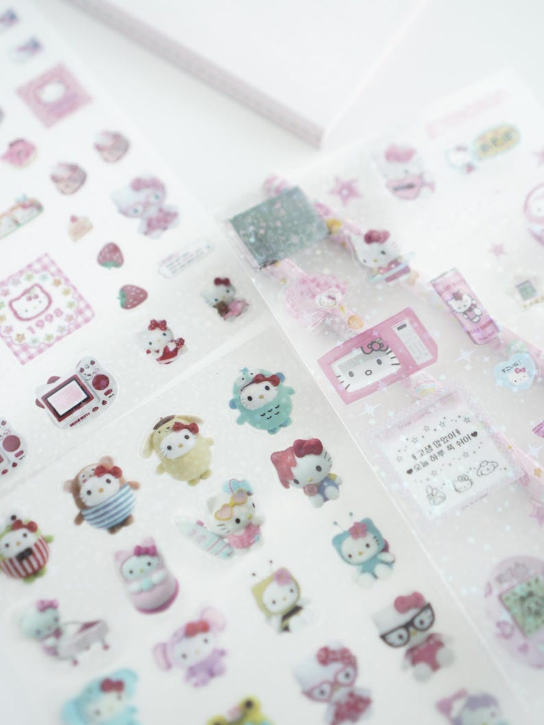 May include: A sheet of clear stickers featuring a variety of Hello Kitty characters. The stickers are pink, white, and blue and feature Hello Kitty in different poses and outfits. The stickers are perfect for adding a touch of whimsy to your planner, journal, or scrapbook.