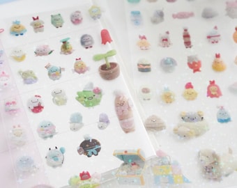 May include: A sheet of clear stickers featuring various cute cartoon characters and objects. The stickers are arranged in rows and columns on a white background. The characters include a variety of animals, plants, and food items. The stickers are perfect for adding a touch of whimsy to your planner, journal, or other craft projects.