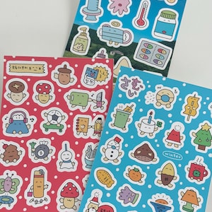 Puede incluir: Tres hojas de pegatinas coloridas con varias ilustraciones de dibujos animados. Una hoja presenta pegatinas con temas médicos, otra tiene personajes caprichosos y la tercera tiene diseños con temas de invierno. Las pegatinas están sobre fondos punteados blancos.