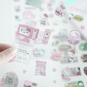 May include: A sheet of clear stickers featuring Hello Kitty characters and objects. The stickers are pink and white and include a microwave, a can of Hello Kitty soda, a boombox, a phone, a star, and a Hello Kitty character holding a bag of marshmallows. The text on the stickers includes "Hello Kitty", "Strawberry Marshmallow", and "오늘은" in Korean.