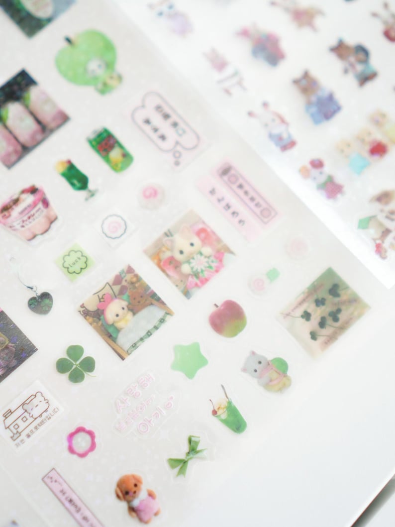 May include: A sheet of clear stickers with various designs, including animals, food, and plants. The stickers are on a white background. The stickers are in pink, green, and white.
