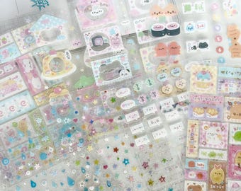 May include: A collection of clear sticker sheets featuring various designs, including stars, raindrops, and cartoon characters. Some stickers have Japanese text. The color palette includes pastel pinks, blues, and yellows.