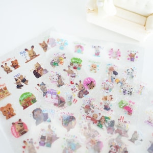 May include: A sheet of clear stickers featuring cartoon animals with Japanese text. The stickers are on a white background and are arranged in rows. The stickers are in a variety of colours and feature different animals, including bears, rabbits, and cats.