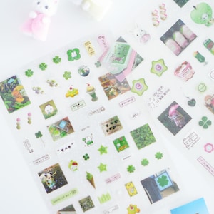 May include: A sheet of clear stickers with various designs, including four-leaf clovers, stars, and small images of animals and plants. The stickers are on a white background.