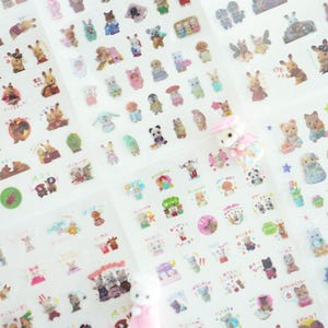 May include: A sheet of clear stickers featuring various cartoon animals, including rabbits, bears, cats, and dogs. The stickers are arranged in rows and columns on a white background. The stickers are all different sizes and shapes, and some of them have Japanese text on them.