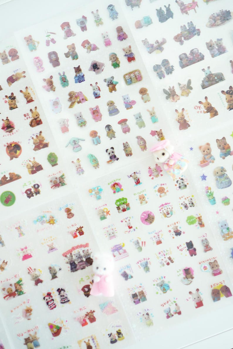 May include: A sheet of clear stickers featuring various cartoon animals, including rabbits, bears, cats, and dogs. The stickers are arranged in rows and columns on a white background. The stickers are all different sizes and shapes, and some of them have Japanese text on them.