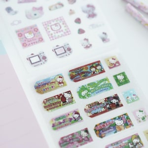 May include: A sheet of Hello Kitty stickers featuring various designs, including Hello Kitty in different outfits and locations, with text in Japanese. The stickers are on a white background.