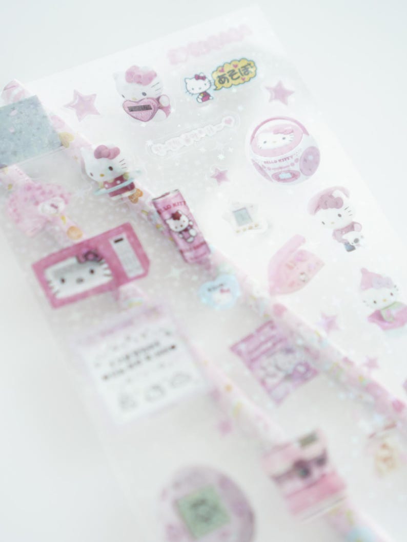 May include: A sheet of pink Hello Kitty stickers with various images including Hello Kitty holding a heart, Hello Kitty in a car, Hello Kitty in a phone, Hello Kitty in a radio, Hello Kitty in a boombox, Hello Kitty in a chain, Hello Kitty in a star, and Hello Kitty in a speech bubble that says "お元気です".