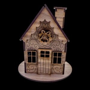 May include: A wooden decorative house with a chimney, windows, and a door. The house features intricate cut-out designs, including hearts and a wreath. It is set on a round wooden base, perfect for holiday decor.