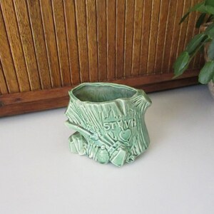 May include: Green ceramic planter shaped like a tree stump with the word "STVH" carved into the side. The planter has a heart shape carved into the side and a small green bird perched on a branch.