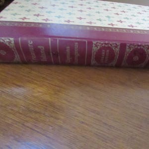 May include: A red hardcover book with gold lettering. The title is "Treasure Island" and the author is "Captain's Courageous". The book is part of a "Library Edition" series.