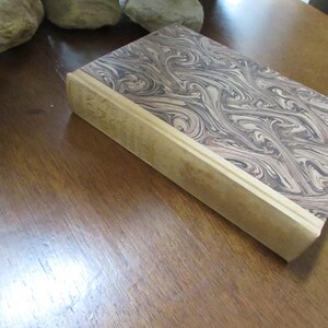 May include: A vintage hardback book with a marbled cover in shades of brown and cream. The spine is cream colored and has gold lettering that reads "The Works of Charles Dickens".