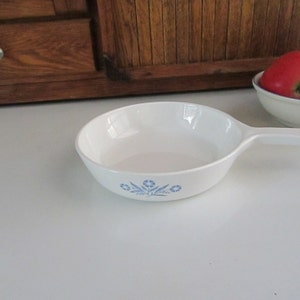 May include: White ceramic skillet with a blue floral design. The skillet has a single handle.