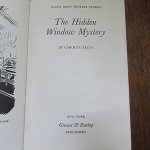 May include: The cover of a Nancy Drew mystery book titled "The Hidden Window Mystery" by Carolyn Keene. The book is published by Grosset & Dunlap in New York.