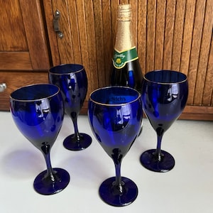 May include: Four cobalt blue wine glasses with gold rims and a bottle of Welch's sparkling grape juice.