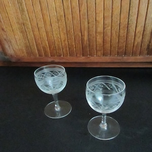 May include: Two clear glass stemmed drinking glasses with etched designs. The glasses have a round bowl and a short stem.
