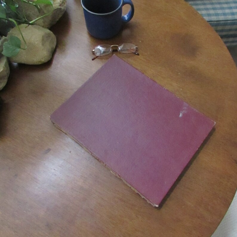 May include: A burgundy hardback book lying flat on a wooden table.