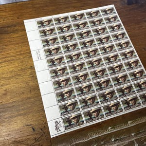 May include: A sheet of postage stamps featuring a portrait of D.W. Griffith. Each stamp has a portrait of a man wearing a hat and holding a camera. The stamps are arranged in a grid on a white sheet, with the text "D.W. GRIFFITH" on each stamp.