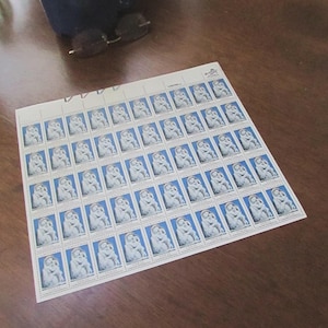 May include: A sheet of postage stamps featuring a white and blue design. Each stamp depicts a seated figure with a child. The stamps are arranged in neat rows and columns on a white sheet.