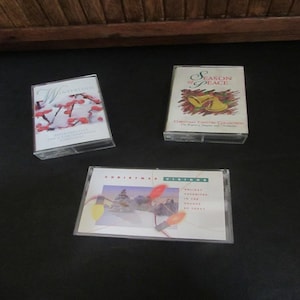 May include: Three cassette tapes with Christmas themes. The first tape is titled "Winterlude" and features a snowy scene with red berries. The second tape is titled "Season of Peace" and features a pair of gold bells. The third tape is titled "Christmas Visions" and features a snowy scene with Christmas lights.