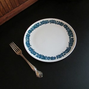 May include: A white ceramic plate with a blue floral border. The plate is on a black surface with a silver fork next to it.