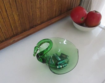 May include: A green glass swan-shaped dish with a heart-shaped bowl. The dish is filled with small green and white candies.