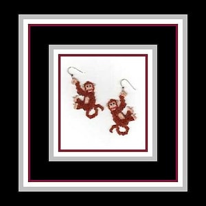 Puede incluir: Un par de pendientes colgantes con un diseño de mono marrón. Los monos se agarran a un alambre plateado y cuelgan de los pendientes.