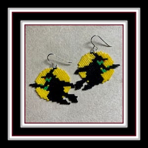 Könnte beinhalten: Ein Paar Hexenohrringe mit schwarzen Hexen, die auf einem gelben Mond fliegen. Die Hexen haben grüne Augen und rote Lippen. Die Ohrringe sind aus Perlen gefertigt.
