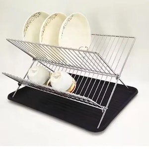 May include: A two-tiered chrome dish drying rack with a black plastic drip tray. The rack is folded and has three white ceramic plates and two white ceramic mugs on it.