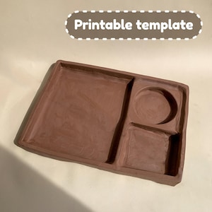 May include: A brown clay tray with three sections. The tray has a large rectangular section, a smaller round section, and a smaller rectangular section.