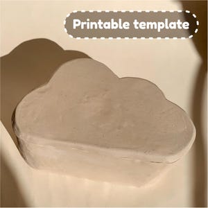 Könnte beinhalten: Eine druckbare Vorlage für eine Box in Wolkenform. Die Vorlage besteht aus einem hellbeigen Material und hat eine glatte Oberfläche.