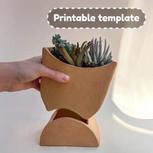 Può includere: Un vaso in ceramica beige dal design curvo unico, contenente una varietà di piante grasse. Il vaso è composto da due parti, una sezione superiore e una base. Il testo "Printable template" è visualizzato in bianco su sfondo marrone.