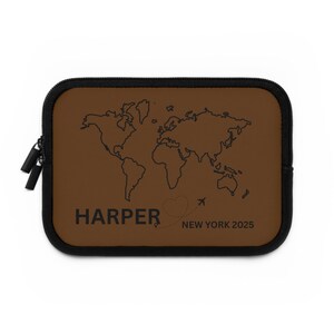 Könnte beinhalten: Eine braune Reisetasche mit schwarzem Reißverschluss und Besatz. Sie zeigt eine Weltkartenumriss und den Namen "HARPER" mit "NEW YORK 2025" darunter gedruckt. Eine gepunktete Linie und ein Flugzeug sind ebenfalls vorhanden.