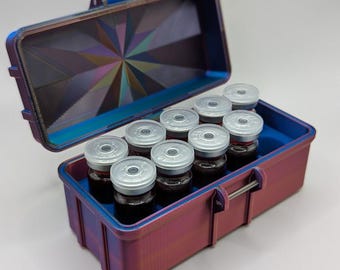 May include: A small, iridescent purple and blue case with a latch, open to reveal a row of ten clear glass vials with silver caps. The case has a geometric pattern on the inside.