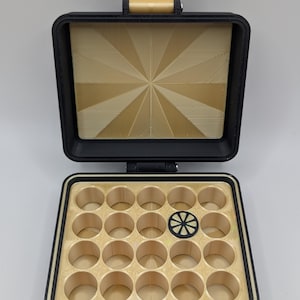May include: A black plastic storage case with a gold interior. The case has a hinged lid and 24 round compartments. The lid has a gold starburst design.