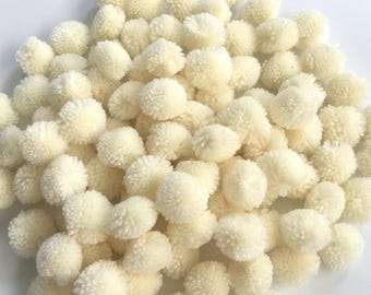 May include: A pile of off-white fluffy pom poms. The pom poms are made of yarn and are about 1 inch in diameter.
