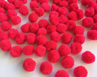 May include: A large group of bright pink fluffy pom poms scattered on a white surface.