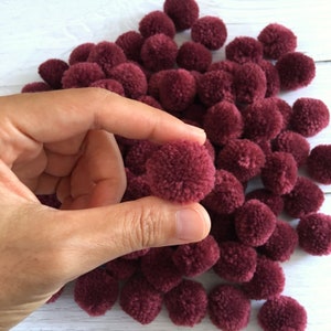 Puede incluir: Un montón grande de pompones burdeos. Los pompones son suaves y esponjosos, y son perfectos para agregar un toque de color y textura a cualquier proyecto artesanal.
