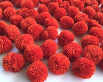 May include: A large group of bright orange fluffy pom poms. The pom poms are arranged in a random pattern on a white background.