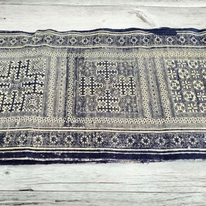 May include: A length of fabric displaying a repeating pattern in navy blue and off-white. The design incorporates geometric shapes, such as crosses and squares, within rectangular panels. The edges are finished with a navy blue border.