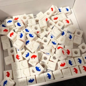 May include: A large pile of white plastic cubes with a red or blue buffalo silhouette on each side. The cubes are scattered in a white box.