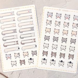 May include: Two sticker sheets featuring cat-themed designs. One sheet has rectangular labels with cat illustrations, and the other has multiple cat faces with bowties and hats. The stickers are in various colors, including gray, beige, and brown. The text "BY HAMA" is at the top.