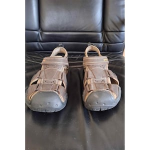 May include: A pair of brown leather sandals with adjustable straps and a black sole. The sandals have a closed-toe design and a hook-and-loop closure for a secure fit. The sandals are designed for outdoor activities and casual wear.