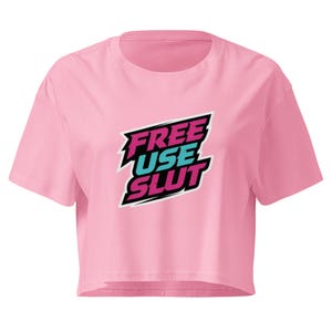 May include: A light pink cropped t-shirt featuring a graphic design with the text "FREE USE SLUT" in a stylised, slanted font. The text "FREE" and "SLUT" are in a vibrant magenta, while "USE" is in a bright cyan, all outlined in black.