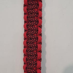 May include: Red and black woven paracord dog collar attachment with silver-colored metal hardware. The attachment is made of red paracord with a black woven pattern in the center. The ends are red leather.