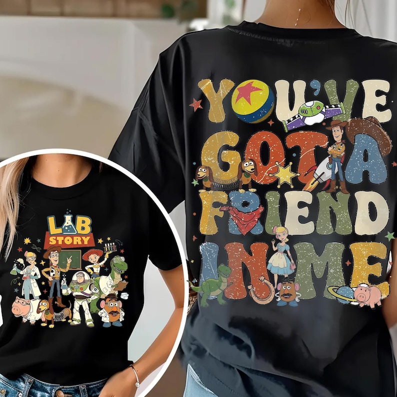 Op de afbeelding: Zwarte T-shirts met Toy Story-personages. E&eacute;n shirt toont "LAB STORY" met figuren, de andere "YOU'VE GOT A FRIEND IN ME" met illustraties. Beide zijn shirts met korte mouwen, geschikt voor casual wear.